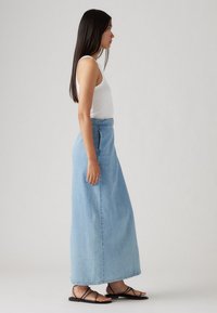 Denim maxi nederdel i lyseblå, med høj talje, lige snit og stiklommer i siden. Båret med en hvid tanktop og sorte sandaler.