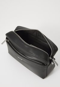 Black leather zippered bag with a smooth texture, featuring a silver zipper and a minimalist design. Interior shows spacious compartments.