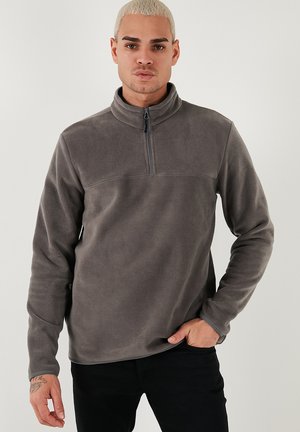 Grå fleece-pullover med lynlås kvart op ad kraven, lange ærmer og en glat tekstur. Accentueret med en simpel søm hen over brystet.