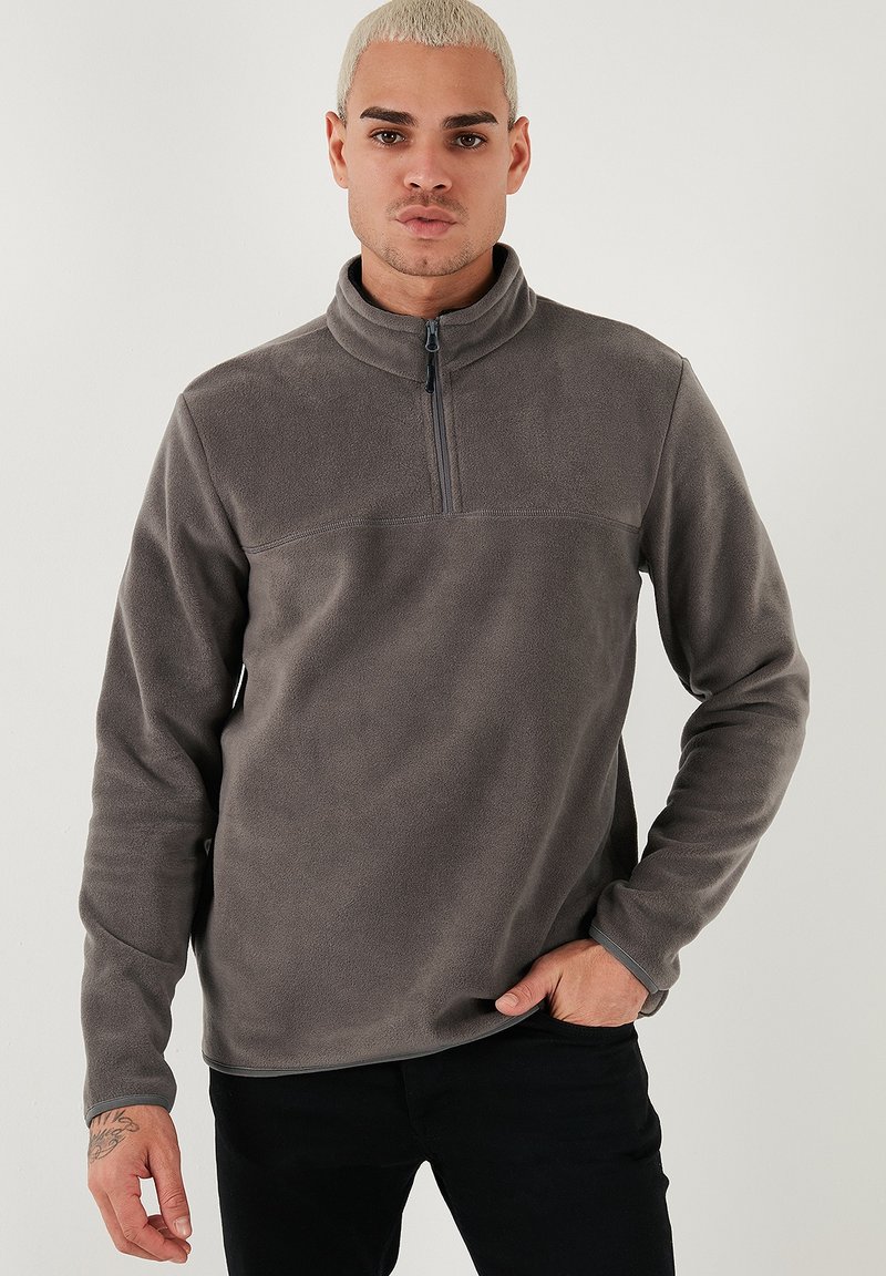 Grå fleece-pullover med lynlås kvart op ad kraven, lange ærmer og en glat tekstur. Accentueret med en simpel søm hen over brystet.