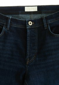 Mörkblå denimjeans med rak passform, framfickor, kontrasterande gula sömmar och en knappstängning i midjan.