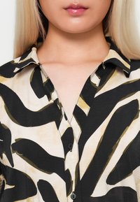 Black and beige shirt with abstract patterns, featuring a collar and black buttons, made of lightweight fabric, smooth texture.