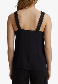 Camisola nera con dettagli in pizzo sulle spalline, con una texture liscia, vestibilità rilassata e orlo posteriore dritto, progettata per il comfort e per essere sovrapposta.