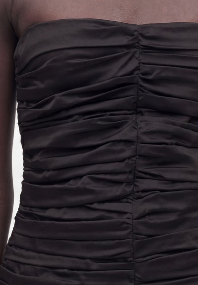 Μαύρο στράπλες σατέν φόρεμα με ρίγες σε άτομο, που δείχνει λεπτομερή υφή και συγκεντρωμένο ύφασμα στο στήθος και τη μέση.