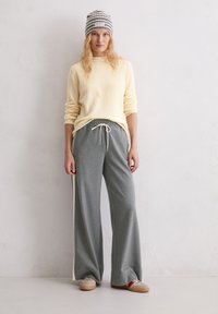 Jasnożółty sweter, szare długie spodnie dresowe z troczkami i szaro-biała czapka w paski. Casualowe obuwie w kolorze beżowym z czerwonym akcentem.