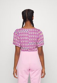 Top a maniche corte con motivo a diamante nei colori viola, rosa e crema. Tessuto liscio, scollatura rotonda e spalle leggermente a sbuffo.