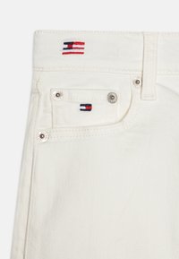 Denim blanco en la cintura con dos bolsillos. Presenta un logo de bandera bordado en rojo, azul y blanco. Detalles en hardware en tono plateado.