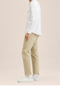 Valkoinen pitkähihainen paita, beige suorat housut ja valkoiset tennarit. Yksinkertainen muotoilu, puuvillakangas, hienostunut rakenne ja klassinen leikkaus.