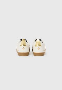 Adidași albi cu accente aurii pe călcâi, căptușeală neagră și tălpi de cauciuc texturate. Au vârful rotunjit și un design minimalist.