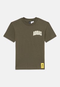 Olivovo zelené bavlnené tričko s krátkymi rukávmi, s bielym logom "ADIDAS" na hrudi a žltou nálepkou na spodnej ľavej strane.