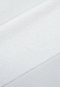 Biała bluza z tkaniny przedstawiająca trzy tekstury: gładką bawełnę, miękki polar i ściągacz prążkowy. Oferuje subtelną różnicę w odcieniach.