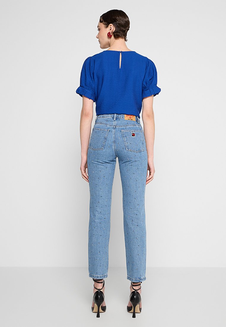 Top corto de manga corta texturizado en azul con un escote en la parte posterior, combinado con jeans de tiro alto en azul claro que presentan sutiles motas de colores y bolsillos traseros.