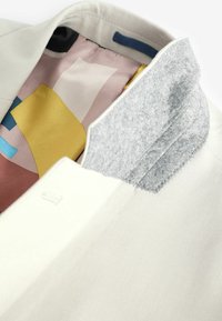 Chaqueta gris claro con un collar texturizado de lana, que cuenta con un forro interior de patrón geométrico colorido en tonos de rosa, amarillo y azul.