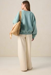 Sweatshirt oversize vert menthe, pantalon large crème, et un sac à épaule beige avec une écharpe à motif nouée au poignet.