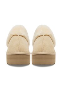 Béžové semišové pantofle s nadýchaným krémově bílým kožíškem, s kulatou špičkou a plochou podrážkou s jemnou texturou.