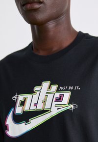 Camiseta de algodón negra con gráfico del logo de Nike en varios colores y el eslogan "JUST DO IT", diseño sencillo de cuello redondo y mangas cortas.