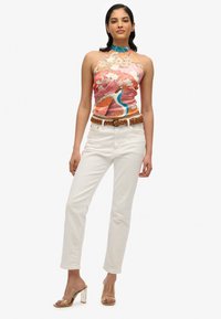 Kleurvolle haltertop met een bloemen- en pauwontwerp, witte rechte broek en sandalen met doorzichtige hakken. Dit outfit heeft een geweven bruine riem.