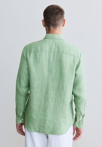 Chemise en lin vert clair à manches longues avec col, poignets boutonnés et ourlet arrondi. Tissu texturé avec une coupe décontractée.
