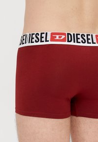Červené bavlnené boxerky so širokým bielym pásom s čiernym logom "DIESEL" a štýlizovaným akcentom "D".