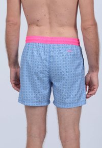 Maillots de bain bleus avec un motif géométrique, taille élastique rose et poches latérales. Tissu léger avec une texture respirante.