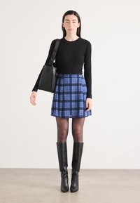 Black long-sleeve shirt, blue plaid skirt, high black boots. Skirt features blue and navy squares, smooth texture with a slight sheen.