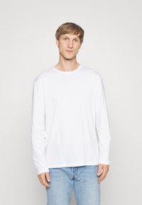 Weißes Langarmshirt aus Baumwolle mit rundem Halsausschnitt und lockerer Passform, kombiniert mit hellblauen Jeans. Minimalistisches Design.