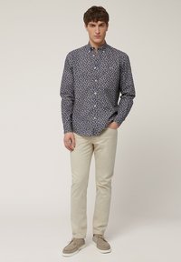 Lange mouwen button-up shirt in donkerblauw met een bloemenpatroon, gecombineerd met lichtbeige chino's en grijze suède schoenen.