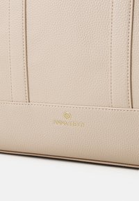Beige textured leather handbag with prominent stitching and a subtle embossed logo. Features a structured design and smooth accents.
