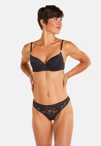 Ensemble de lingerie en dentelle noire comprenant un soutien-gorge rembourré avec des motifs de feuilles, des bretelles ajustables et un string taille basse assorti avec des motifs floraux.