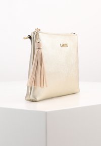 Guldmetallic håndtaske med tekstureret overflade, lynlåslukning og en beige frynseaccent. Har et logo i guldskrift på fronten.