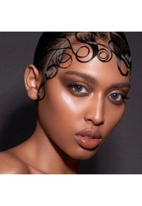 Primer plano de un rostro con piel suave y bronceada. Presenta acentos de cabello liso y rizado, maquillaje de ojos audaz y labios nude brillantes.