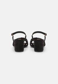 Sandali con tacco alto in suede nero, con un ampio tacco a blocco, cinturino alla caviglia regolabile e design open-toe caratterizzato da dettagli incrociati.