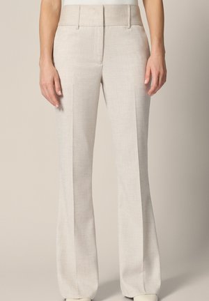 Beżowe spodnie z wysokim stanem i szerokimi nogawkami z przednią plisą, szlufkami na pasek oraz bocznymi kieszeniami, noszone przez osobę na jasnym tle.