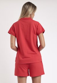 Camiseta polo roja de manga corta, con textura suave y un ajuste relajado, combinada con unos pantalones cortos rojos a juego, creando un conjunto coordinado.