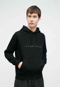 Čierna mikina s kapucňou a bielym logom "JACK & JONES", sťahovacia kapucňa, klokanie vrecko, bavlnený materiál a rebrované manžety.