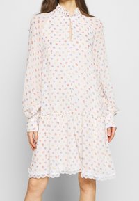 Robe à manches longues en tissu léger et transparent avec une base blanche, ornée d'un motif floral en orange, violet et jaune. Dentelle au niveau de l'ourlet.