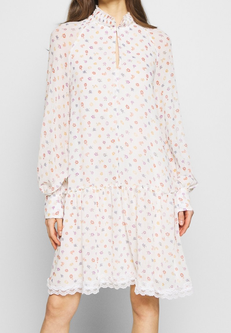 Robe à manches longues en tissu léger et transparent avec une base blanche, ornée d'un motif floral en orange, violet et jaune. Dentelle au niveau de l'ourlet.