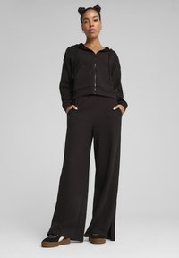 Black zip-up cropped hoodie with a front pocket, paired with wide-leg black pants. Smooth fabric with a relaxed fit. Black platform sneakers.