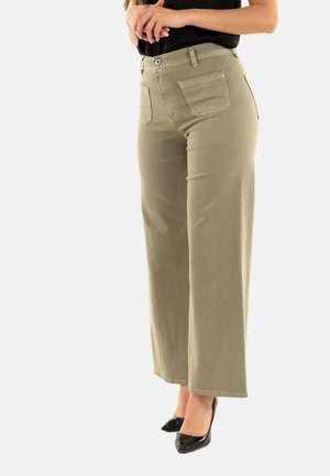 Pantalons évasés en coton vert olive ; taille haute avec poches avant ; texture lisse, design simple ; associés à des escarpins noirs à bout pointu.