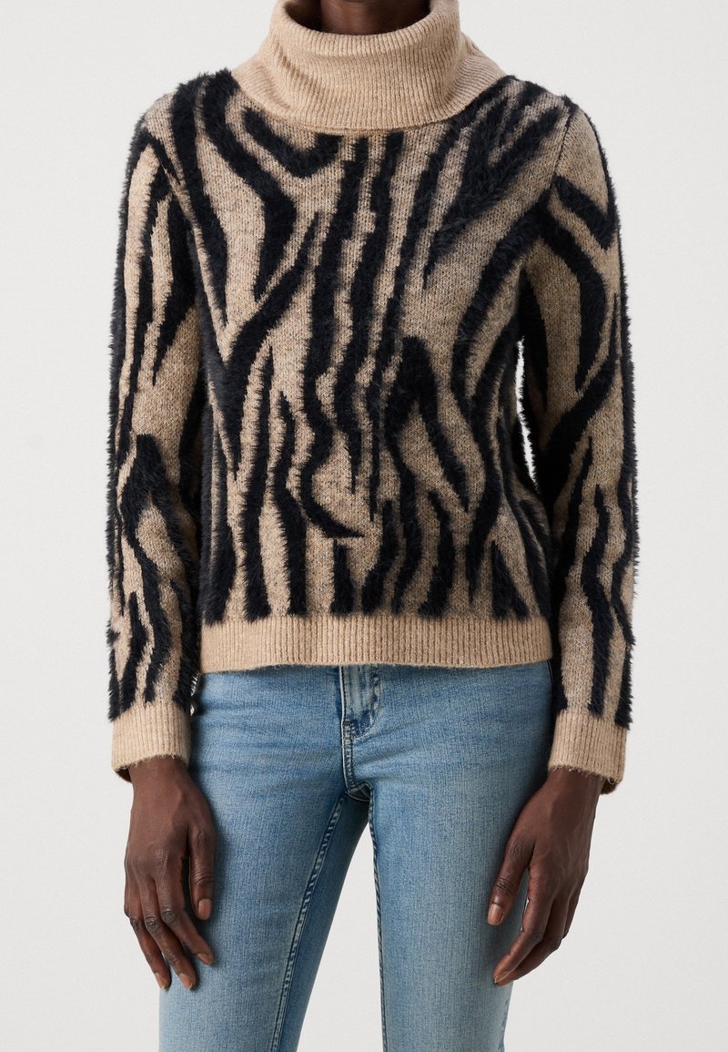 Beige tröja med ett svart fluffigt zebramönster, med hög hals, långa ärmar och ribbad mudd. Mjuk textur och avslappnad passform.