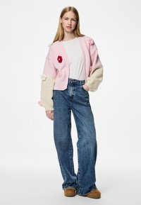 Ροζ και κρεμ oversized πουλόβερ με λουλουδένια κεντήματα, σε συνδυασμό με ψηλόμεσα μπλε τζιν. Διαθέτει ραμμένα μανίκια και βαθύ V-λαιμό.