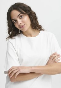 T-shirt bianca in cotone con maniche corte e colletto rotondo. Il tessuto appare liscio con una vestibilità rilassata, presentato su uno sfondo neutro.