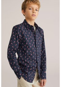 Mörkblå skjorta med ett upprepat mönster av polkagrisar i rött och vitt. Den har krage i klassisk stil och långa ärmar.