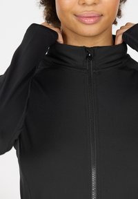 Zwarte zip-up jas met hoge kraag, gemaakt van gladde, rekbare stof. Heeft een voorkant met rits en een aansluitend ontwerp.