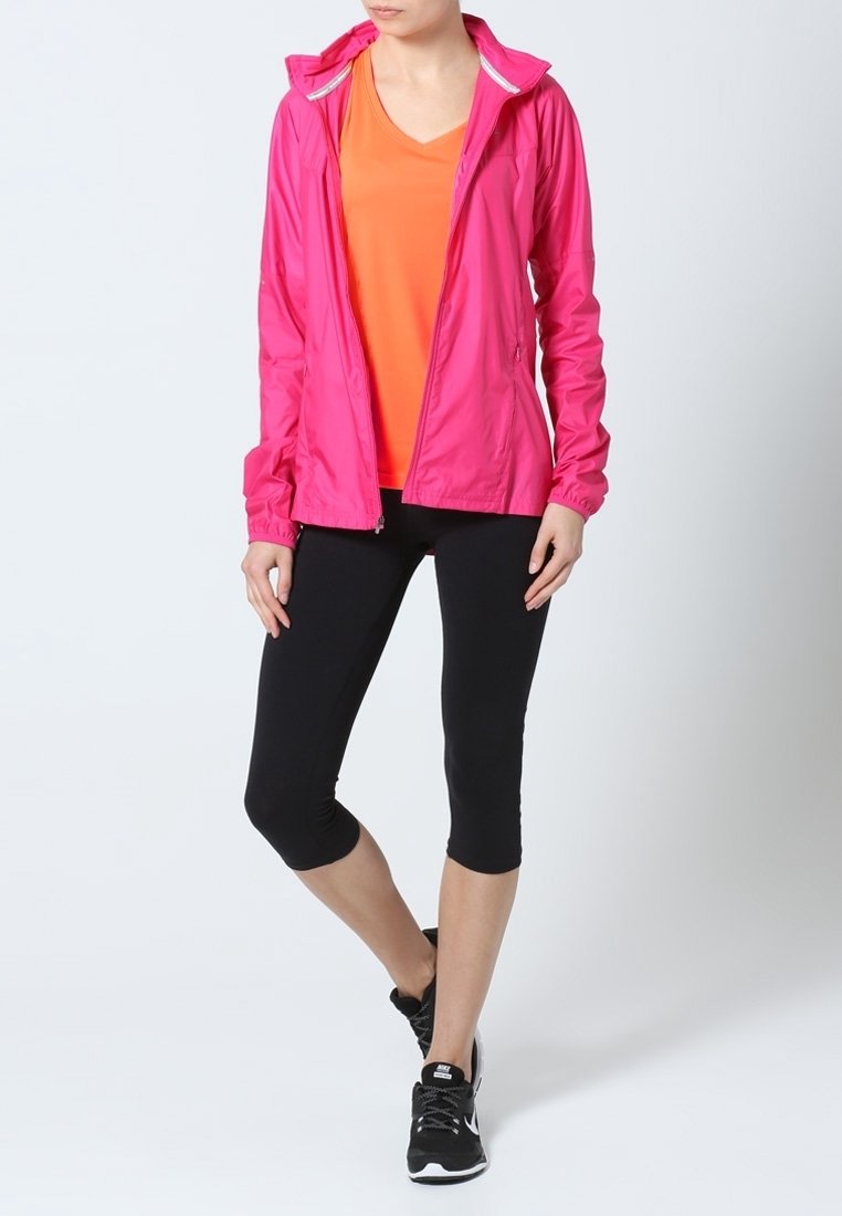 Rosa lättviktig jacka med huva, orange t-shirt under, svarta capri leggings och svarta träningsskor. Slät tyg och åtsittande design.