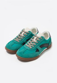 Zapatillas de ante en color verde azulado con acentos en negro, cordones texturizados en color blanco roto, un collar en color crema y una suela de goma marrón.