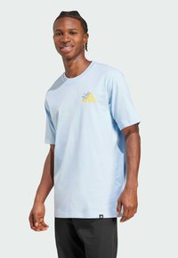 Světle modré bavlněné tričko s krátkým rukávem, s žlutým grafickým designem na levé části hrudi. Černý logo akcent na lemu.