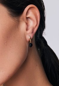Złote kolczyki w kształcie obręczy z czarnym, sferycznym zawieszeniem, z teksturowanymi akcentami i polerowanym wykończeniem.