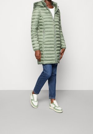 Lichtgroene pufferjas met capuchon, met verticale naden, rits aan de voorkant en zijzakken. Gecombineerd met blauwe jeans en sneakers met groene accenten.