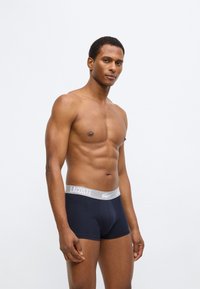 Boxer en coton bleu marine avec une ceinture grise ornée du logo Lacoste, présentant une coupe ajustée et une texture lisse.